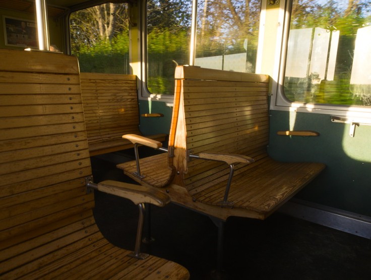 Sièges de train vintage en bois dans la lumière du soleil couchant, le paysage défile derrière les vitres du train